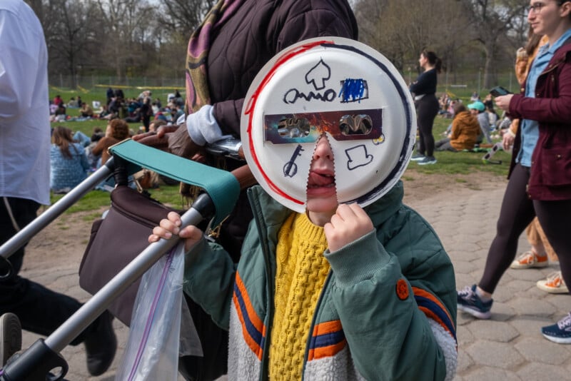 A child wears a paper plate mask with eclipse lenses.