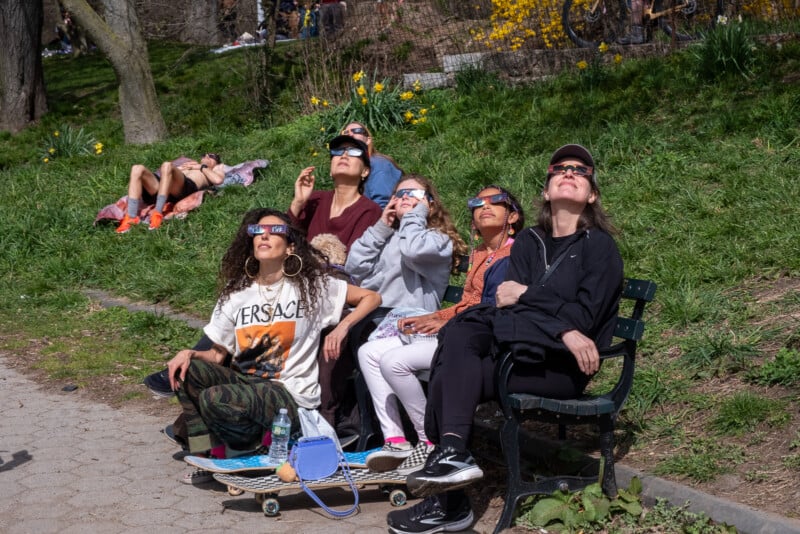 A group of friends looks up at the sky wearing eclipse glasses.