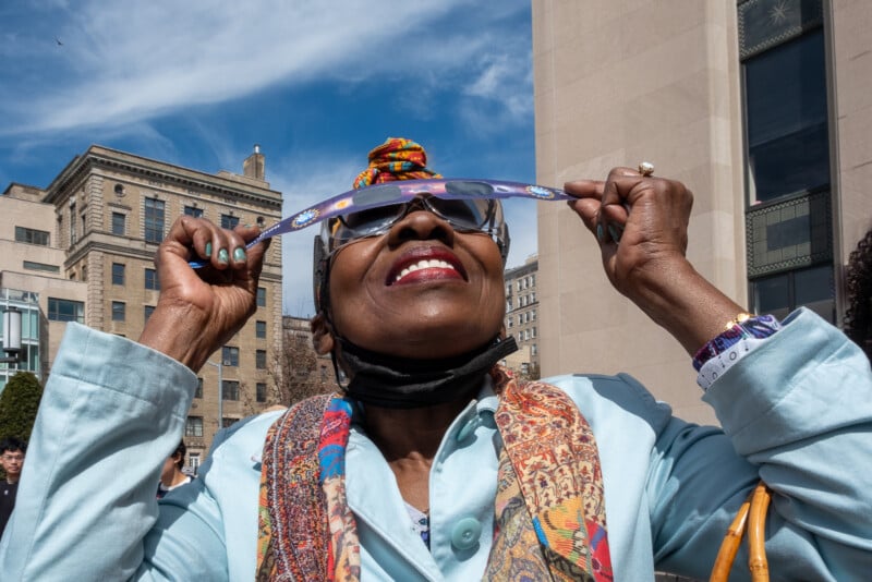 A woman looks up at the sky wearing eclipse glasses.