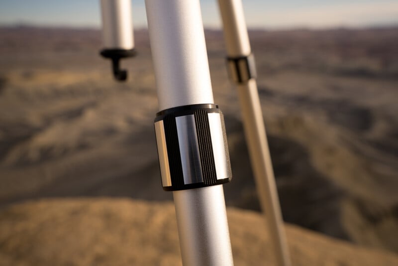 Close-up of a tripod leg with a landscape background, showcasing a mountainous desert terrain under a clear sky.