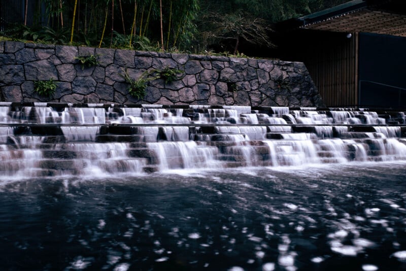 A serene image of a tiered water feature with cascading steps, surrounded by dark stones and green bamboo, creating a tranquil ambiance.