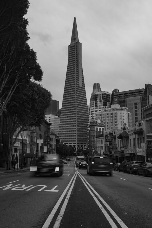 Black and white photo of a city street leading towards the transamerica pyramid in san francisco, with cars moving and victorian-style buildings on each side.
