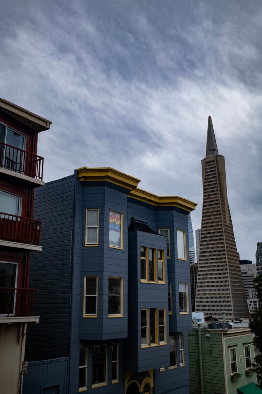 A cityscape with contrasting architecture: colorful modern residential buildings in the foreground and the iconic, sharp-edged transamerica pyramid in the background under a cloudy sky.