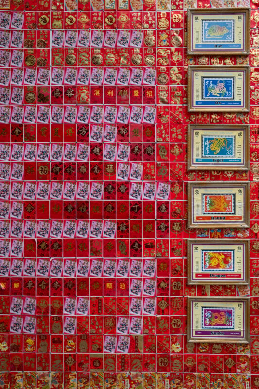 Wall covered with a pattern of red chinese new year envelopes interspersed with vibrant posters depicting traditional scenes and chinese characters.