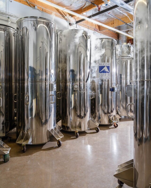 A row of tall, shiny cylindrical tanks on wheels, labeled "alcor," positioned in a well-lit industrial room with exposed ceiling beams.