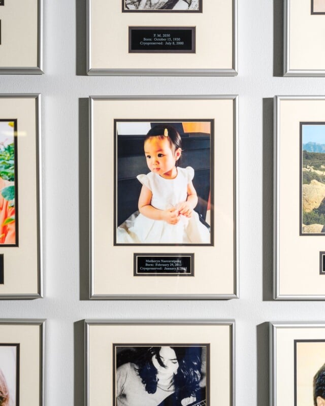 A framed photo of a young child in a white dress on a gallery wall, surrounded by other framed photographs. a small plaque below the image provides details of the artwork.