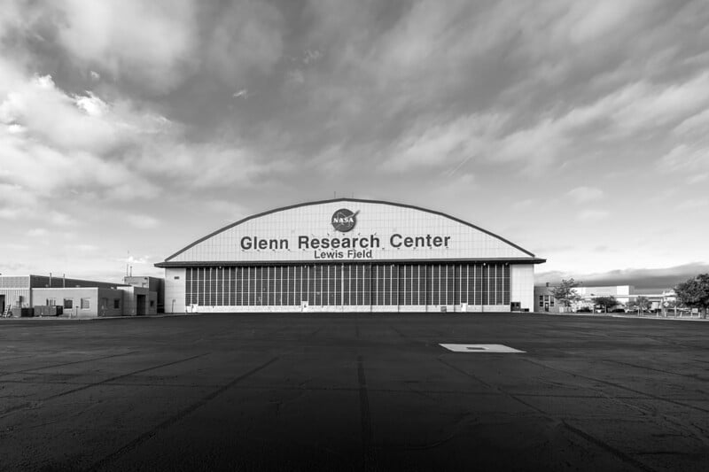 Black and white image of the exterior of nasa's glenn research center at lewis field, featuring a large hangar with a curved roof and the nasa logo prominently displayed.