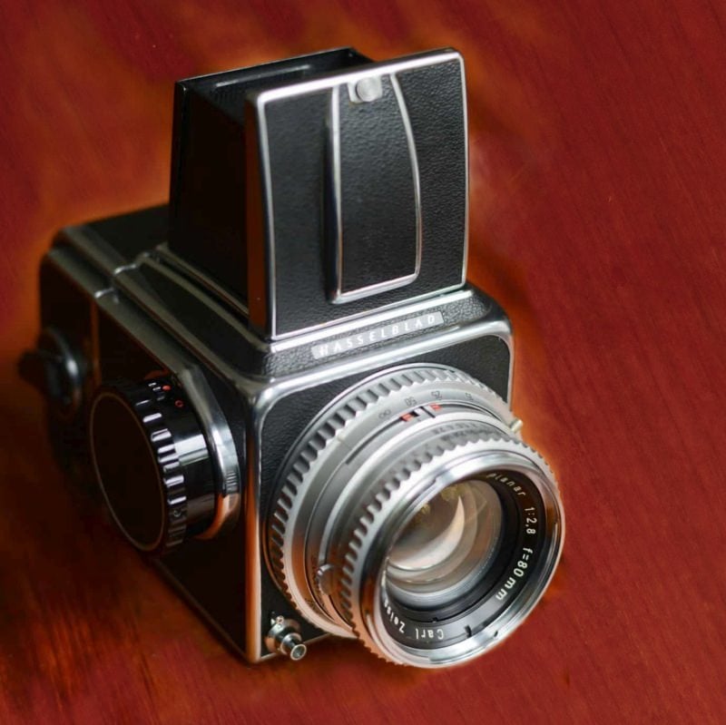 A vintage hasselblad medium format camera with a silver lens, focusing rings, and a waist-level viewfinder, set against a polished wooden background.