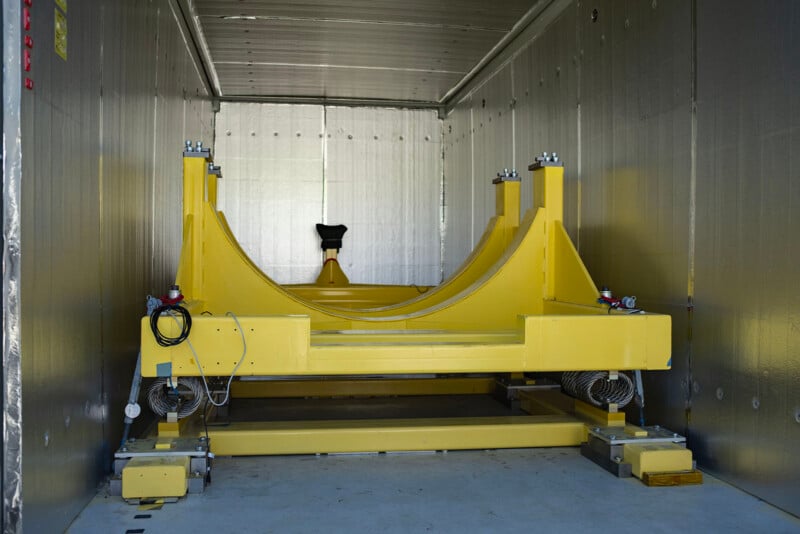Interior of a large metal container with a bright yellow industrial machinery installed at the center, featuring structural supports and electronic components.