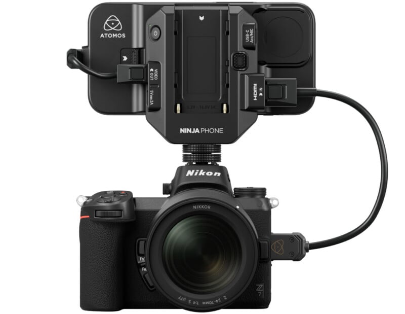 A nikon mirrorless camera with a large lens attached to an atomos ninja recording monitor mounted on top, connected by cables. the setup is displayed against a white background.