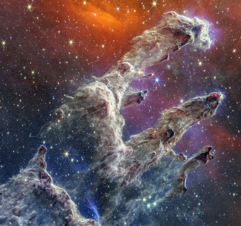 This image depicts a detailed close-up of the pillars of creation, seen in deep space with vibrant hues of blue and orange starlight illuminating the gaseous structures.