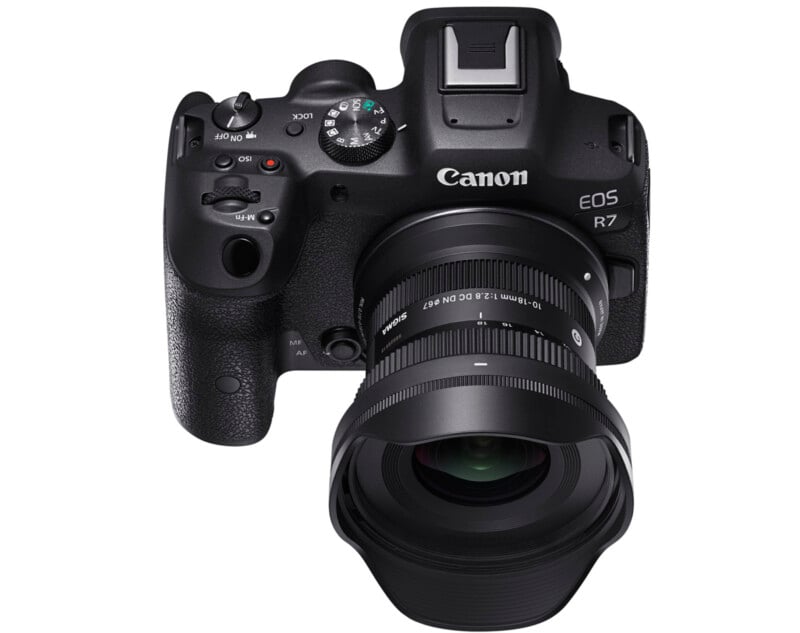 A canon eos r7 mirrorless camera with a large lens attached, viewed from the front. the camera has several control dials and buttons on top and around the grip.