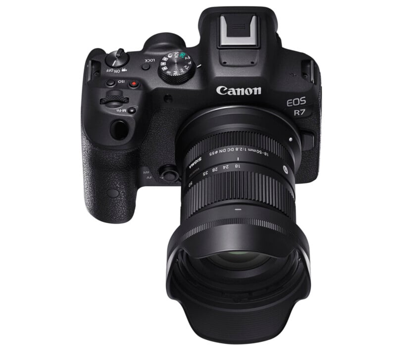 A top view of a canon eos r7 camera featuring a black body and a zoom lens, displaying various control dials and buttons on the top plate.