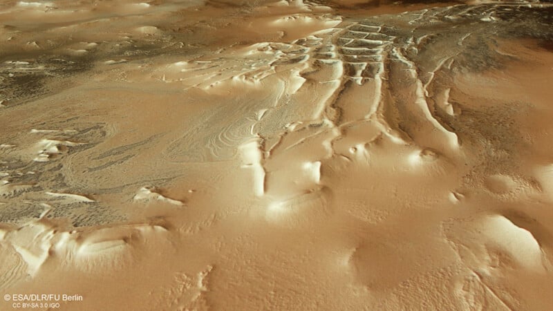 Aerial view of a mars landscape showing intricate patterns of dunes and textured sand formations, depicted in various shades of brown and tan.