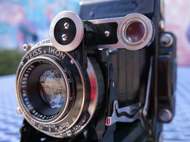Close-up of a vintage zeiss ikon folding camera with its lens and intricate details clearly visible, set against a softly blurred background.