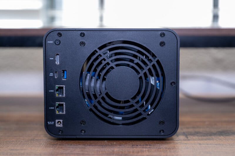 A compact black external computer casing with multiple ports, including usb and ethernet, and a large central cooling fan, placed on a wooden surface.