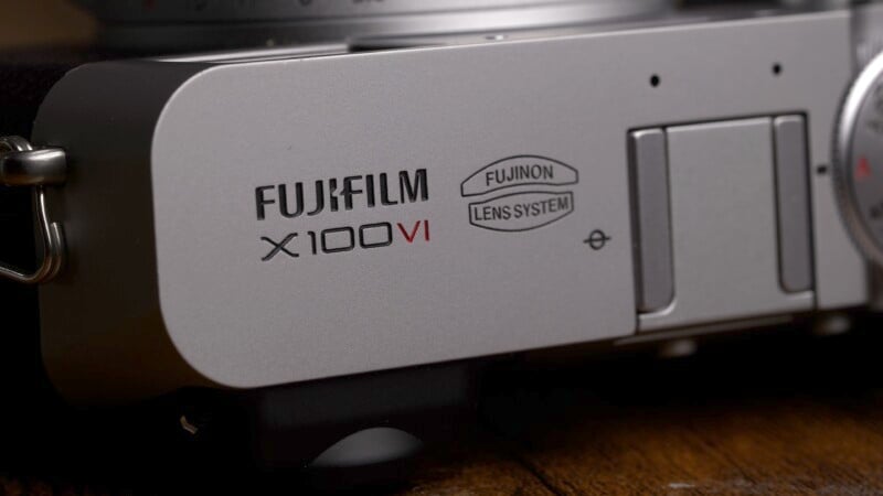 Close-up view of a fujifilm x100v camera focusing on the lens system label and body detail, set against a blurred dark background.