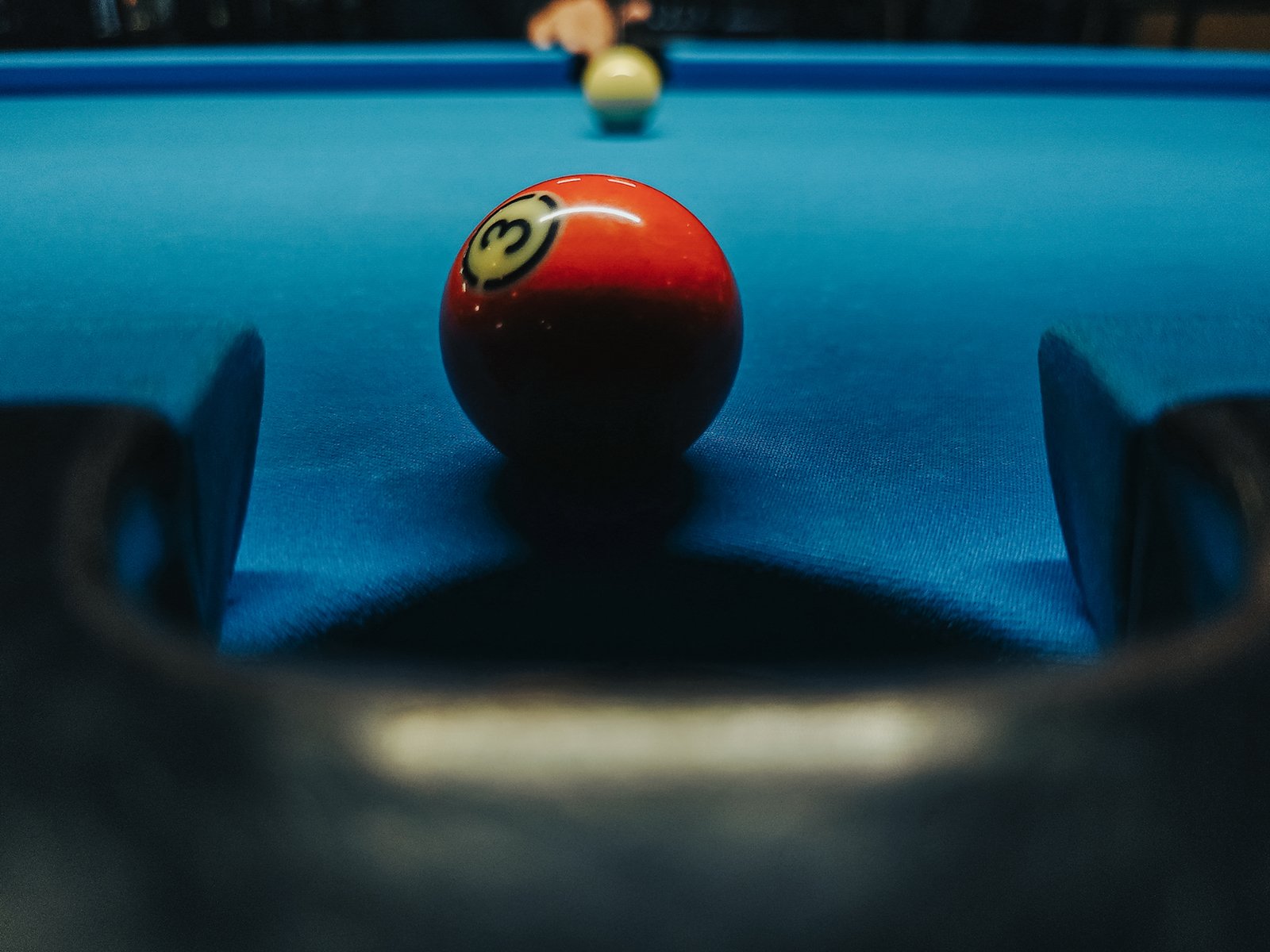 A close-up photo of a billiards table with a red number 3 ball near the pocket and a blurry white ball in the background, implying motion towards the red ball.