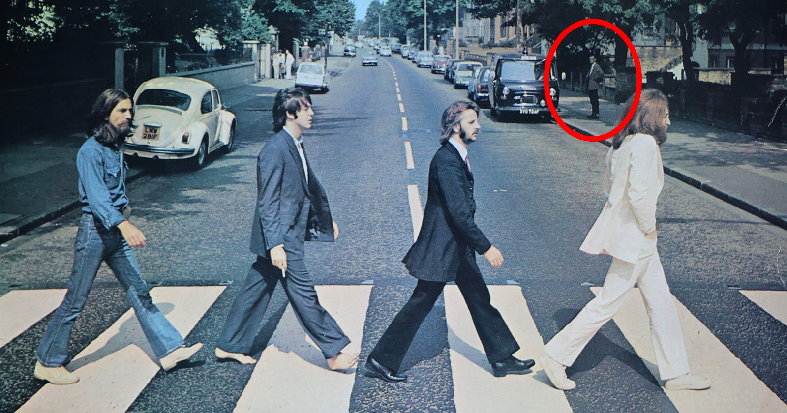 Four men crossing a zebra crossing on a street, with one of them circled in red. cars are parked on both sides of the road, under a clear sky.