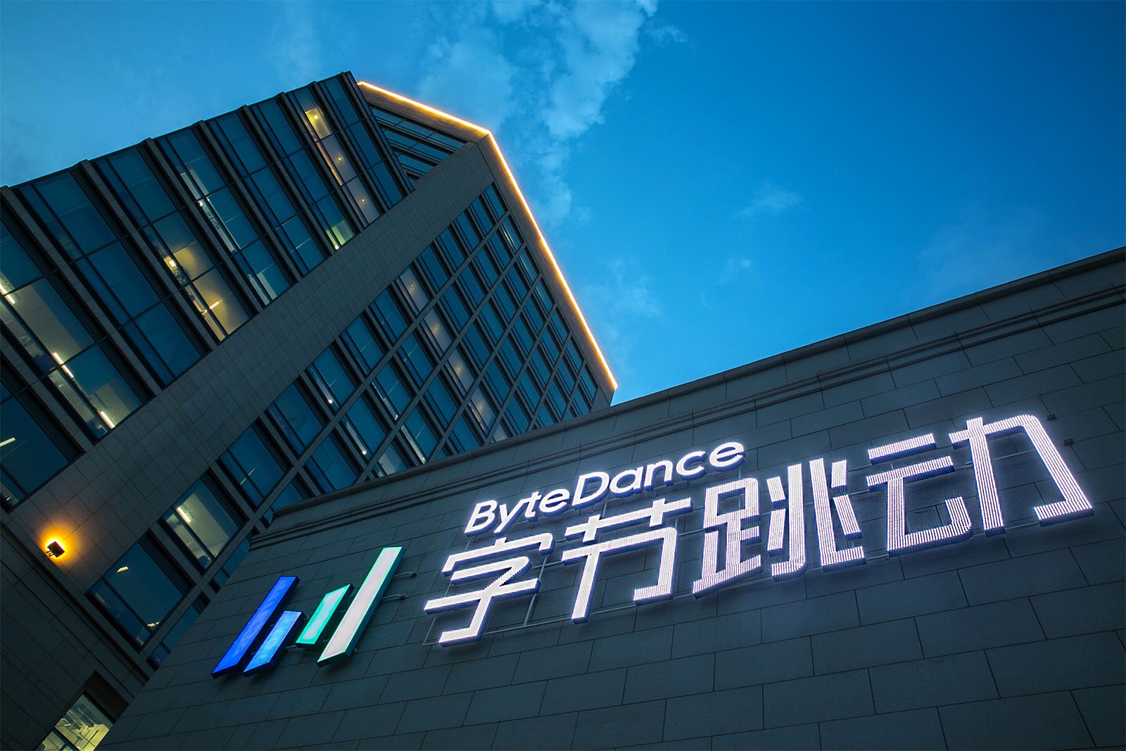 The exterior of a bytedance office building at twilight, featuring the company's logo illuminated in blue and white lights on a modern facade.