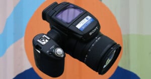 A sony camera with a zoom lens, displayed against a multi-colored circular background. the focus is on the camera's professional features and design details.