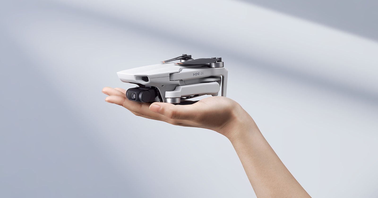A person's hand holding a compact white drone with a camera, set against a soft gray background.