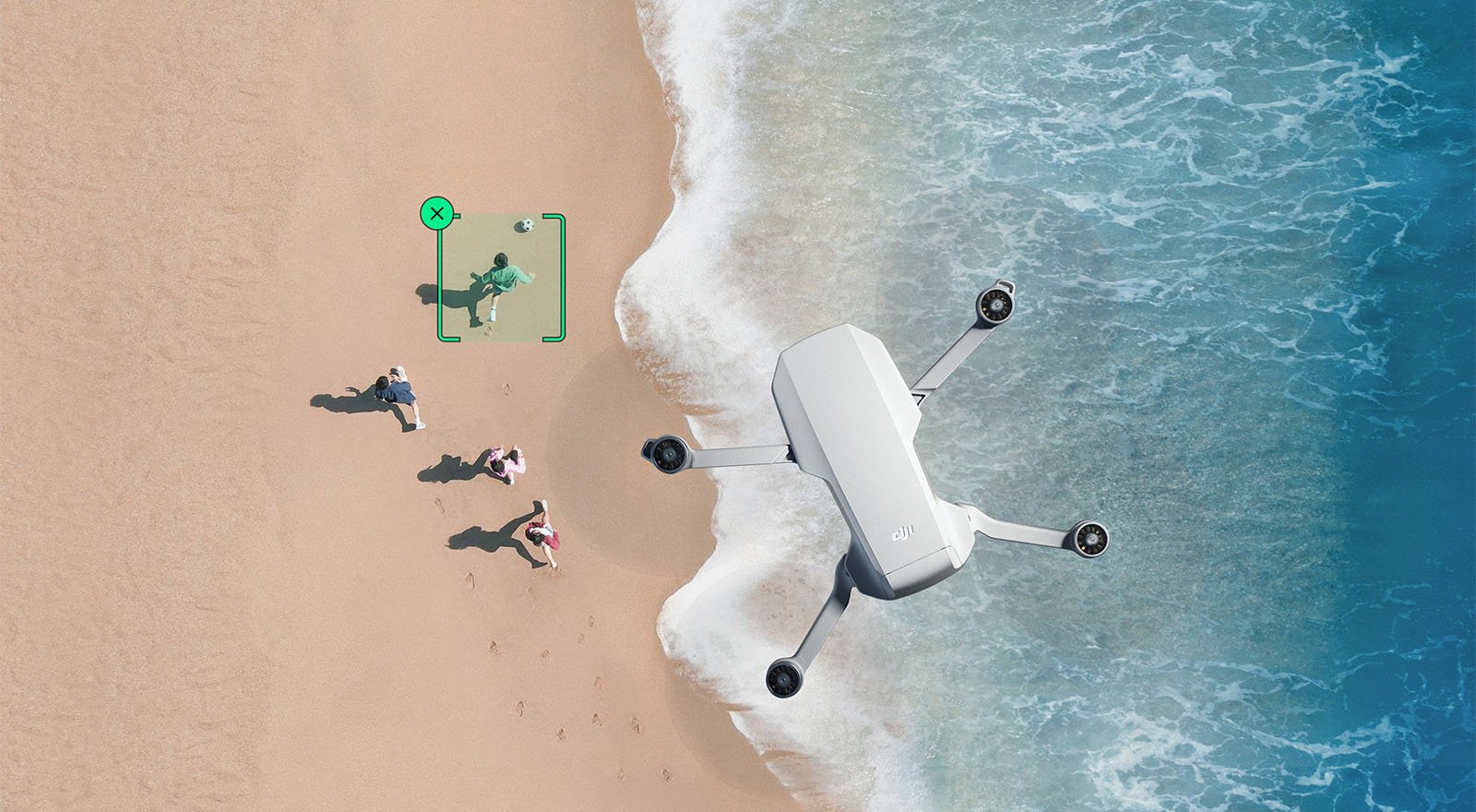 An aerial view of a sandy beach with waves gently lapping at the shore. a large drone is positioned on the sand, surrounded by people looking at it. a person sits on a green mat nearby, operating the drone.