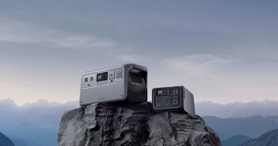 Two portable power stations of different sizes placed on a rocky surface with a mountainous backdrop under a cloudy sky.