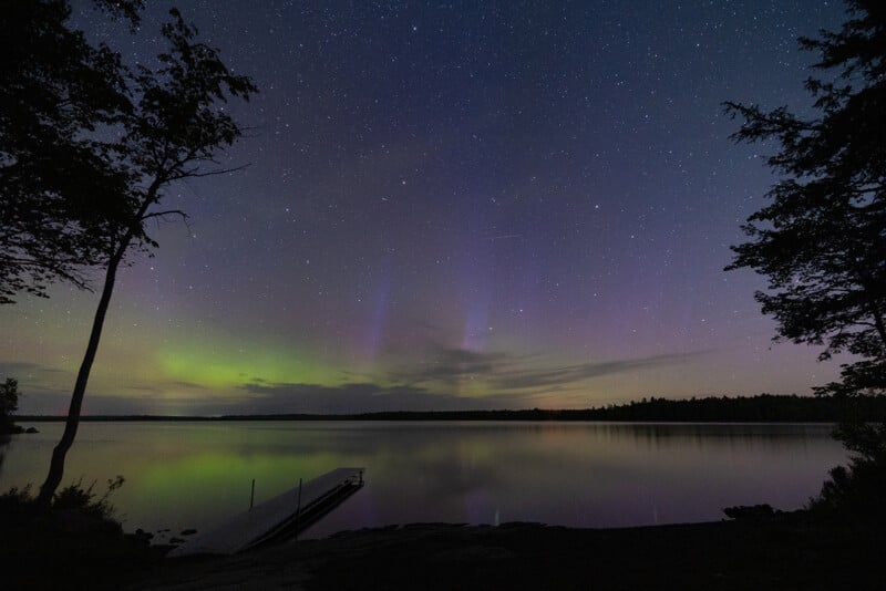 Northern lights are on display over a lake with a dock. 