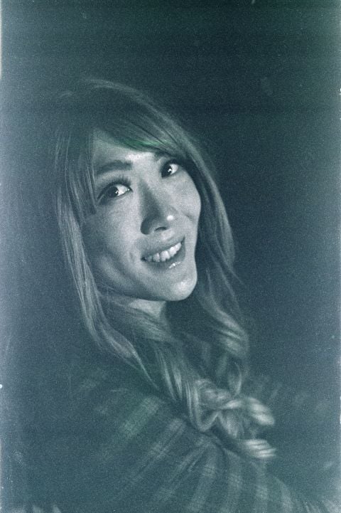 Vintage black and white photo of a smiling woman with long hair, wearing a plaid garment, looking slightly upward and to the side.