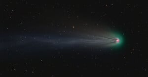 A vivid image of a comet moving through the starry night sky, featuring a bright green nucleus and a long, detailed tail extending across the view.