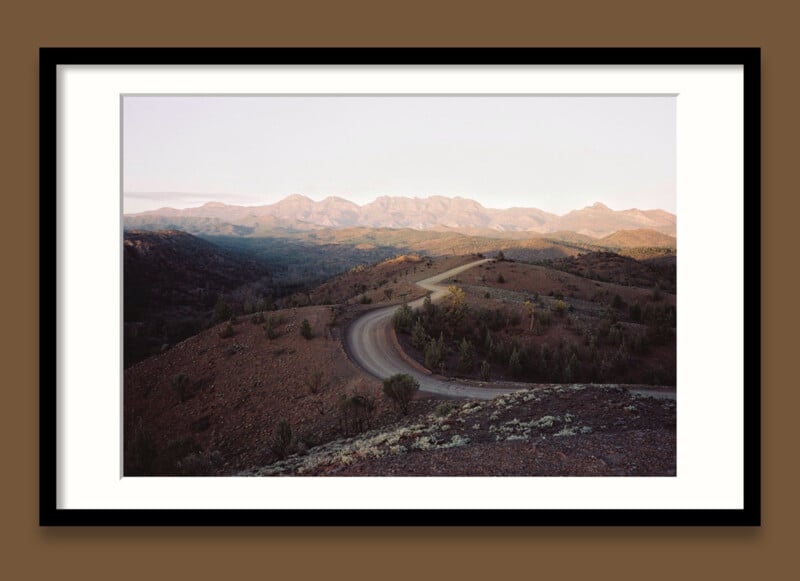 A framed image of a road cutting through desert mountains. 