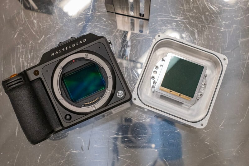 A hasselblad camera with its sensor exposed next to a detached large sensor on a scratched metallic surface.