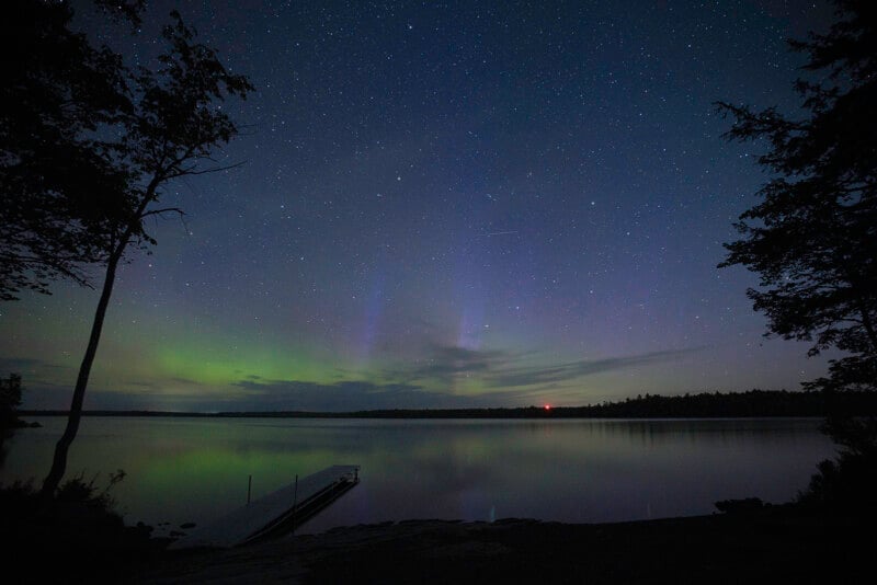 Northern lights are on display over a lake with a dock.