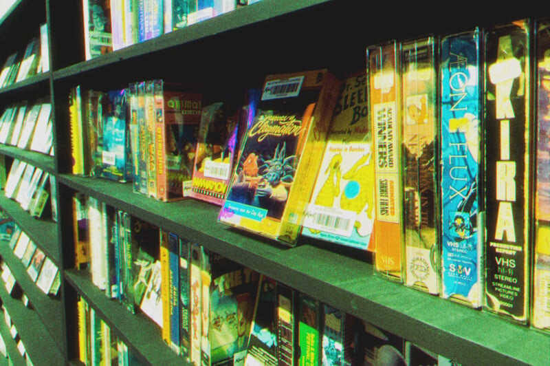 Shelf filled with vintage vhs tapes, including titles such as "dragonheart" and "contra," in colorful cases, displayed in a dimly lit room.