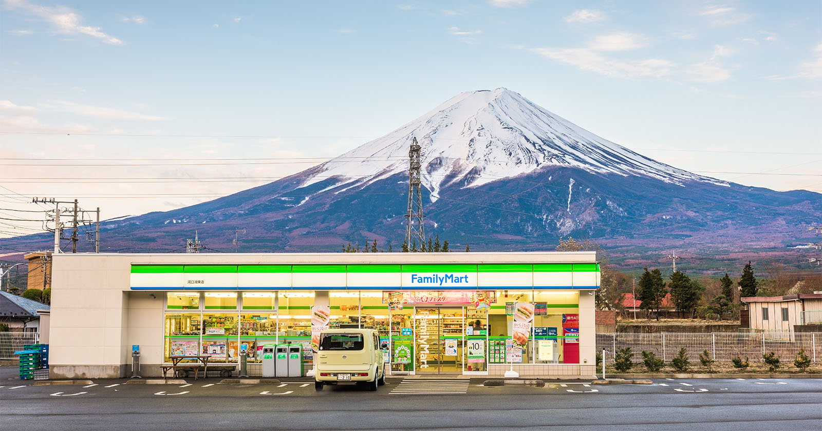 A familymart convenience store in the foreground with mount fuji, its peak covered in snow, majestically rising in the background under a clear sky.
