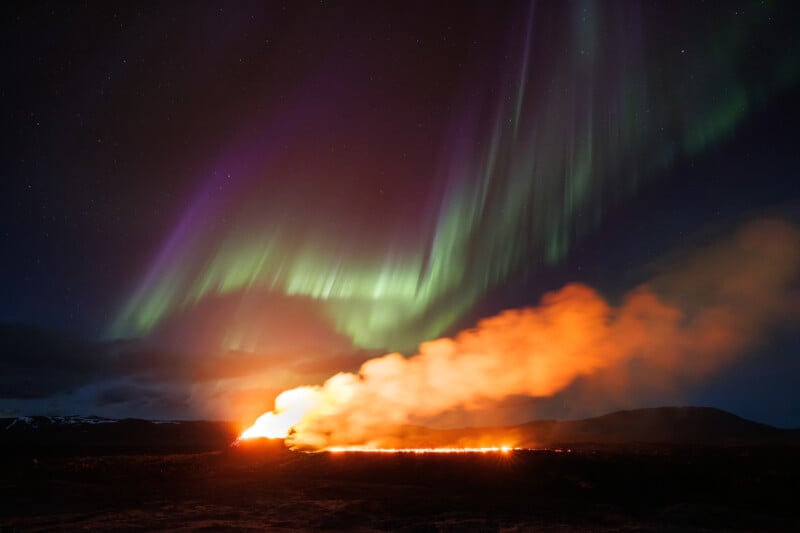 A vivid scene displaying the northern lights in the sky above a fiery volcanic eruption at night, illuminating the dark landscape with radiant colors.