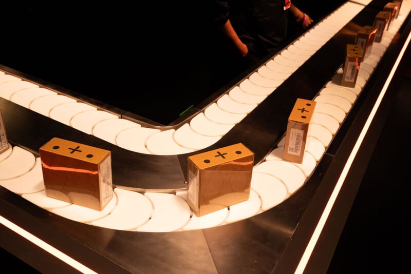 Curved conveyor belt displaying Rabbit R1 boxes, illuminated by warm lights in a dimly lit environment.