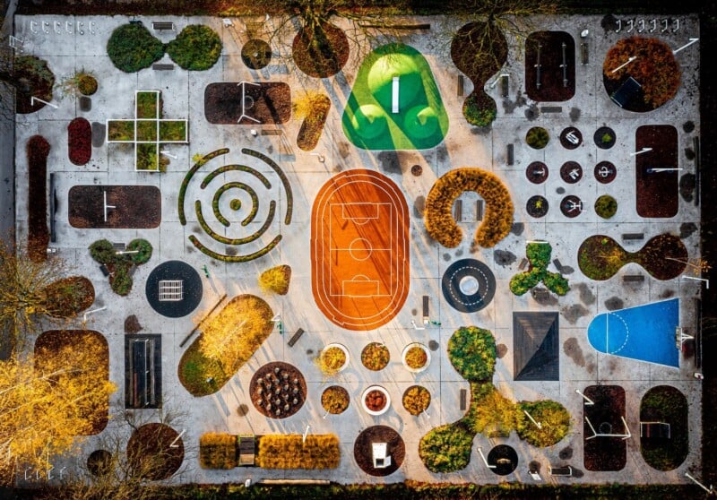 Aerial view of a colorful community garden with various sections including a basketball court, a playground, and diverse plant beds, all arranged in a decorative and organized pattern.