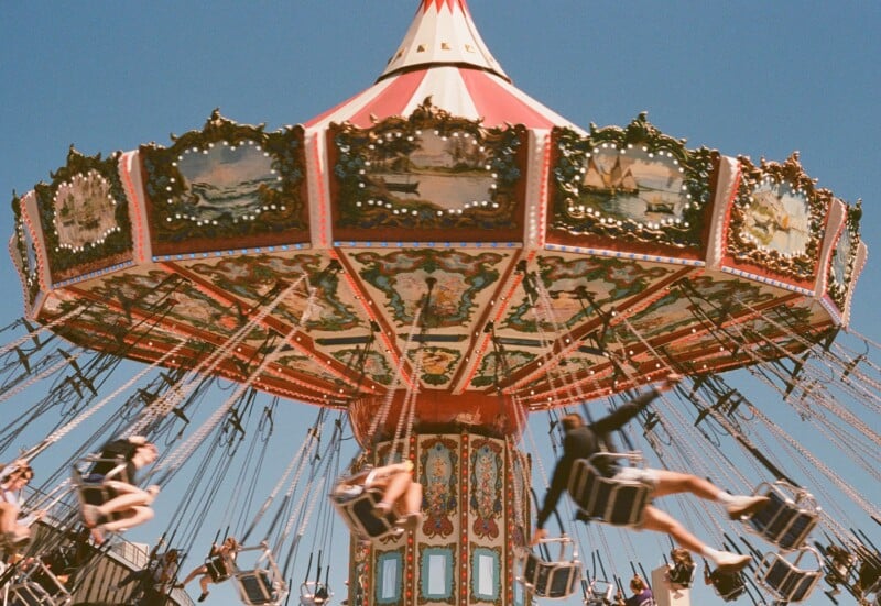 A vibrant, fast-moving carousel swing ride at an amusement park, with people joyfully riding on suspended chairs under a bright blue sky.