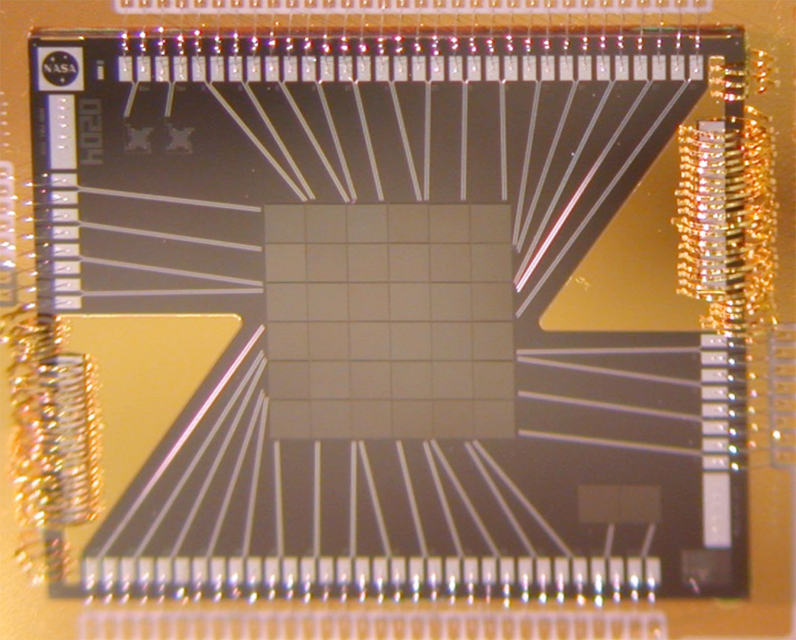 Close-up image of a microprocessor chip showing intricate patterns of circuits, connectors, and a central grid-like structure, mounted on a board with labeling.