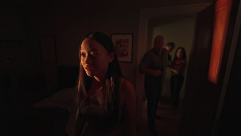 A young woman in a dimly lit room looks anxiously towards a light source, as three blurred figures stand ominously in the background.