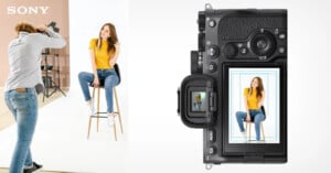 A professional photographer taking a picture of a female model seated on a stool in a studio, depicted conceptually through a sony camera's lcd screen showing the focused photo.