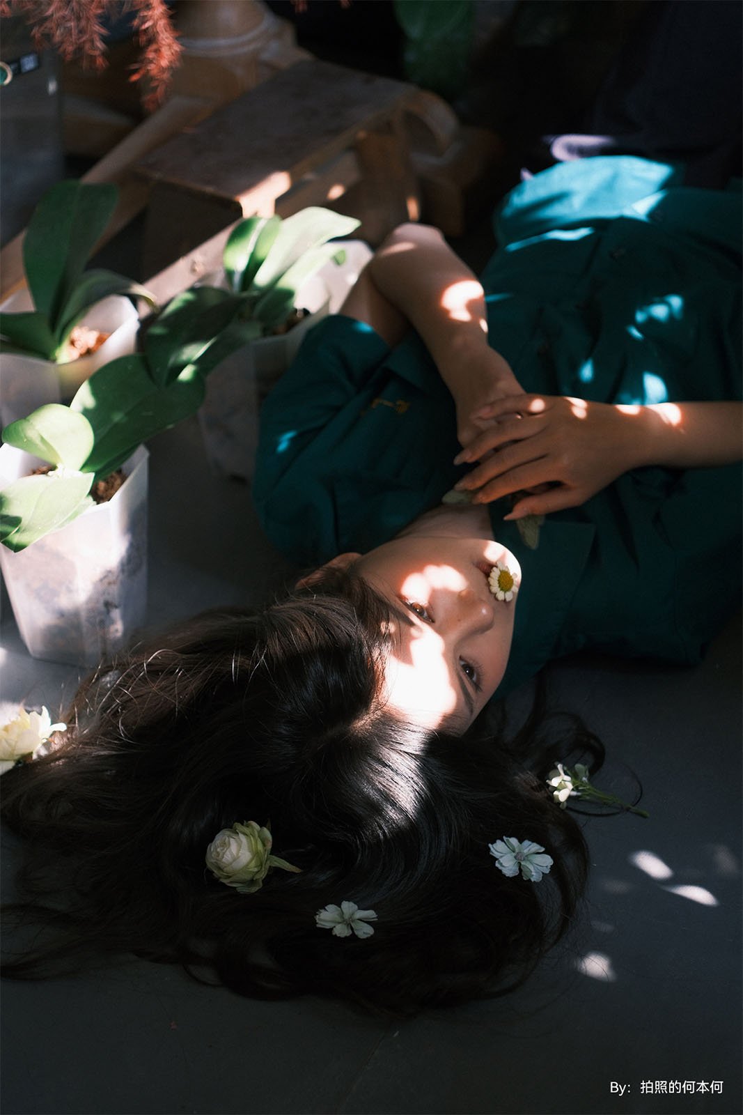 A woman lying on the floor with white flowers in her dark hair, sunlight casting shadows around her, dressed in a teal dress. tranquil and artistic atmosphere.