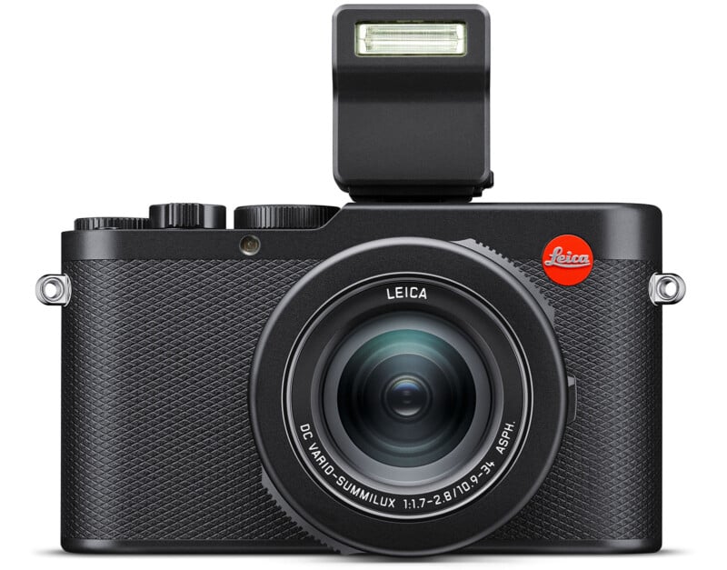 A black Leica digital camera with a textured grip and large lens. The flash is extended above the body, and the red Leica logo is prominently displayed on the top right. The lens is labeled "DC VARIO-SUMMILUX 1:1.7-2.8/10.9-34 ASPH.