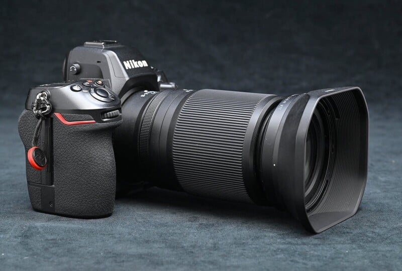 A Nikon digital SLR camera with a large zoom lens is placed against a dark background. The camera has a black body, and the lens features a textured grip and a lens hood. The Nikon logo is visible on the body.