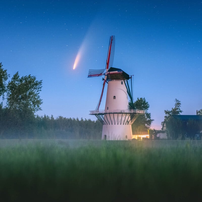 A traditional Dutch windmill stands under a night sky, illuminated by the glow of a comet with a long tail. Mist hovers over a lush green field in the foreground.