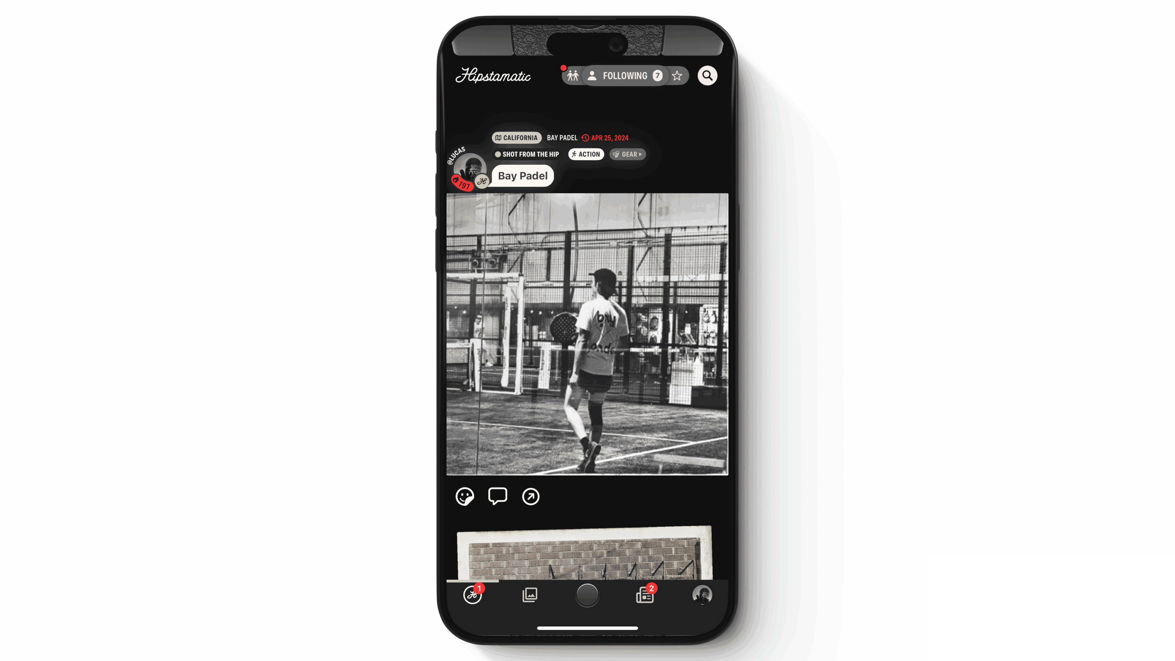 A smartphone displaying a social media app interface with a black and white photo of a man playing basketball in a gym, visible onscreen. icons for likes, comments, and shares are at the bottom.