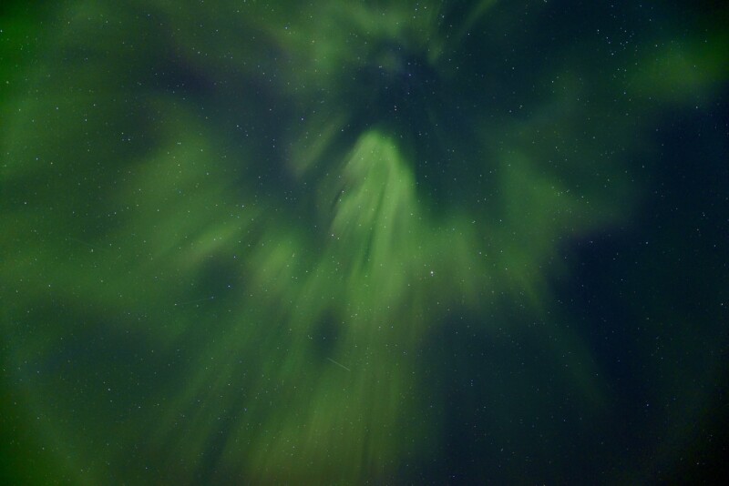 A captivating image of the northern lights displaying vibrant green hues against a starry night sky, with light rays dramatically radiating outward from a central point.