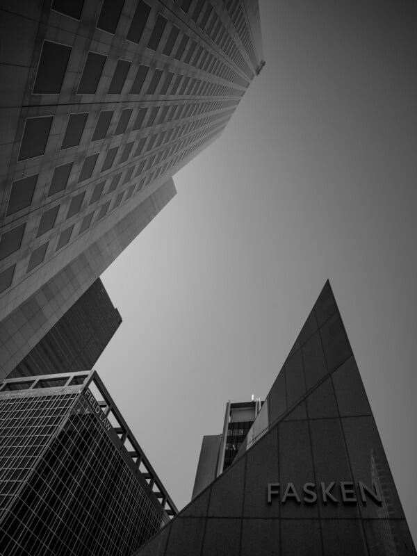 Black and white image looking up at towering skyscrapers with sharp geometric shapes dominating the frame. the name "fasken" is visible on one building.